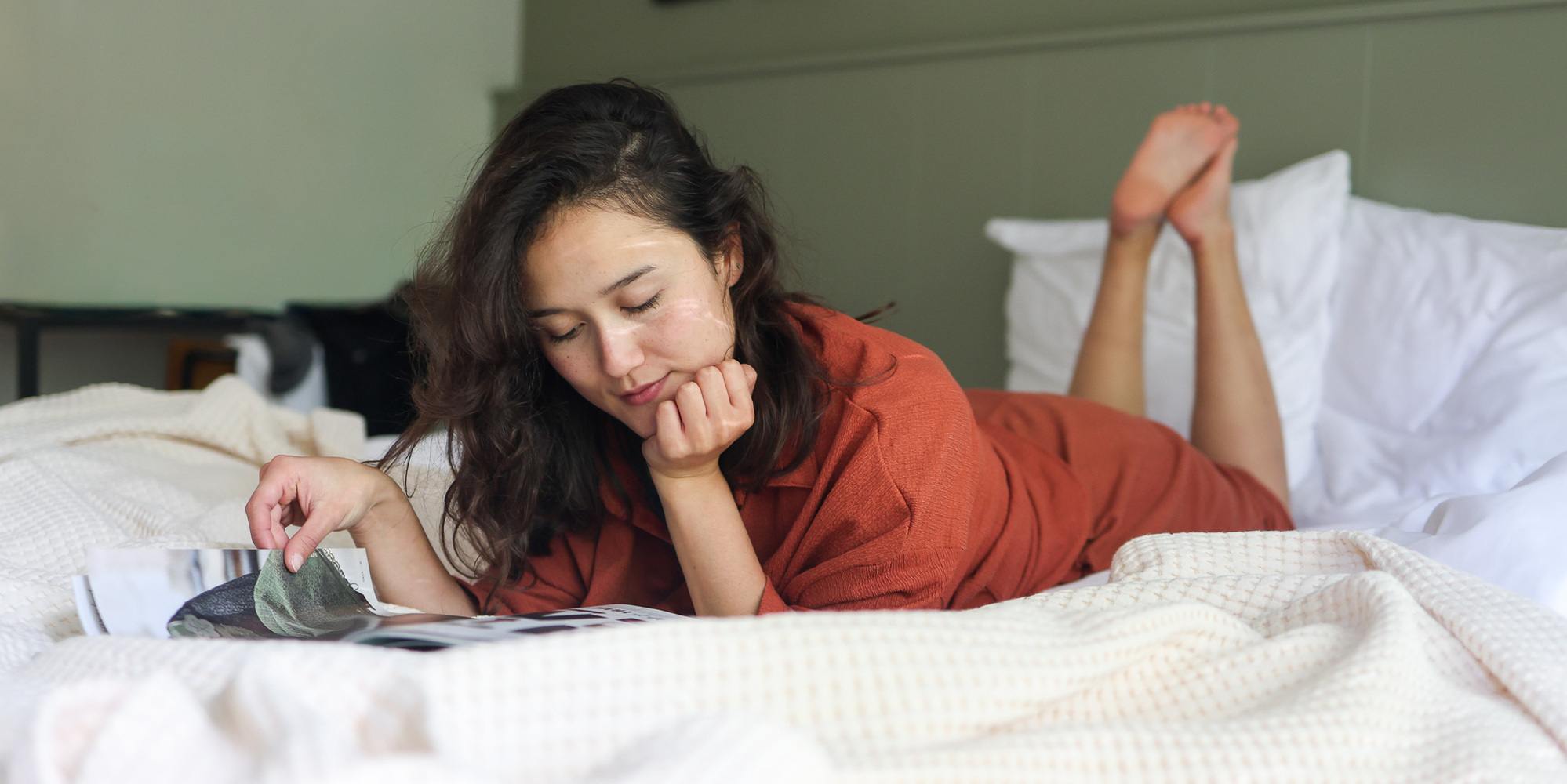 Vrouw in een oranje pyjama die in tijdschrift leest op bed
